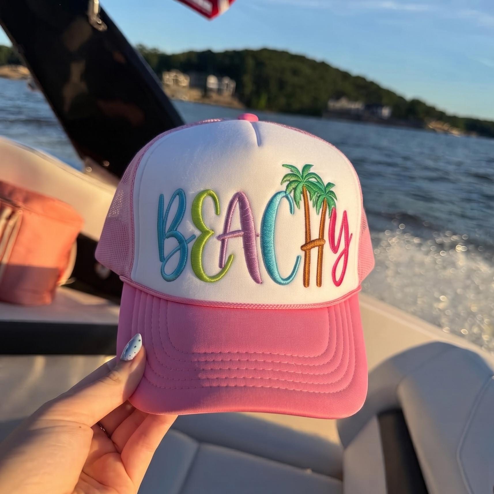 Pink and white beach trucker hat with colorful BEACH embroidery and palm trees on a boat