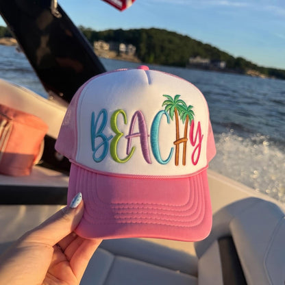 Pink and white beach trucker hat with colorful BEACH embroidery and palm trees on a boat