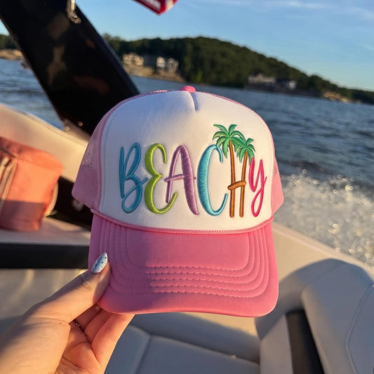 Pink and white beach trucker hat with colorful BEACH embroidery and palm trees on a boat