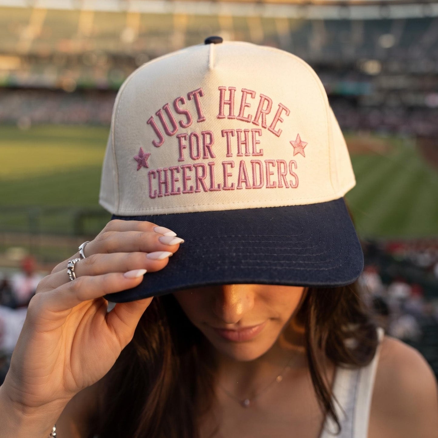 Person wearing a light crown and dark brim Just Here for the Cheerleaders embroidered hat