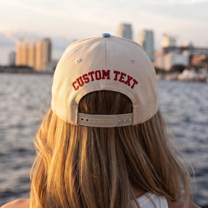 Back view of beige custom text baseball cap with adjustable closure by the waterfront