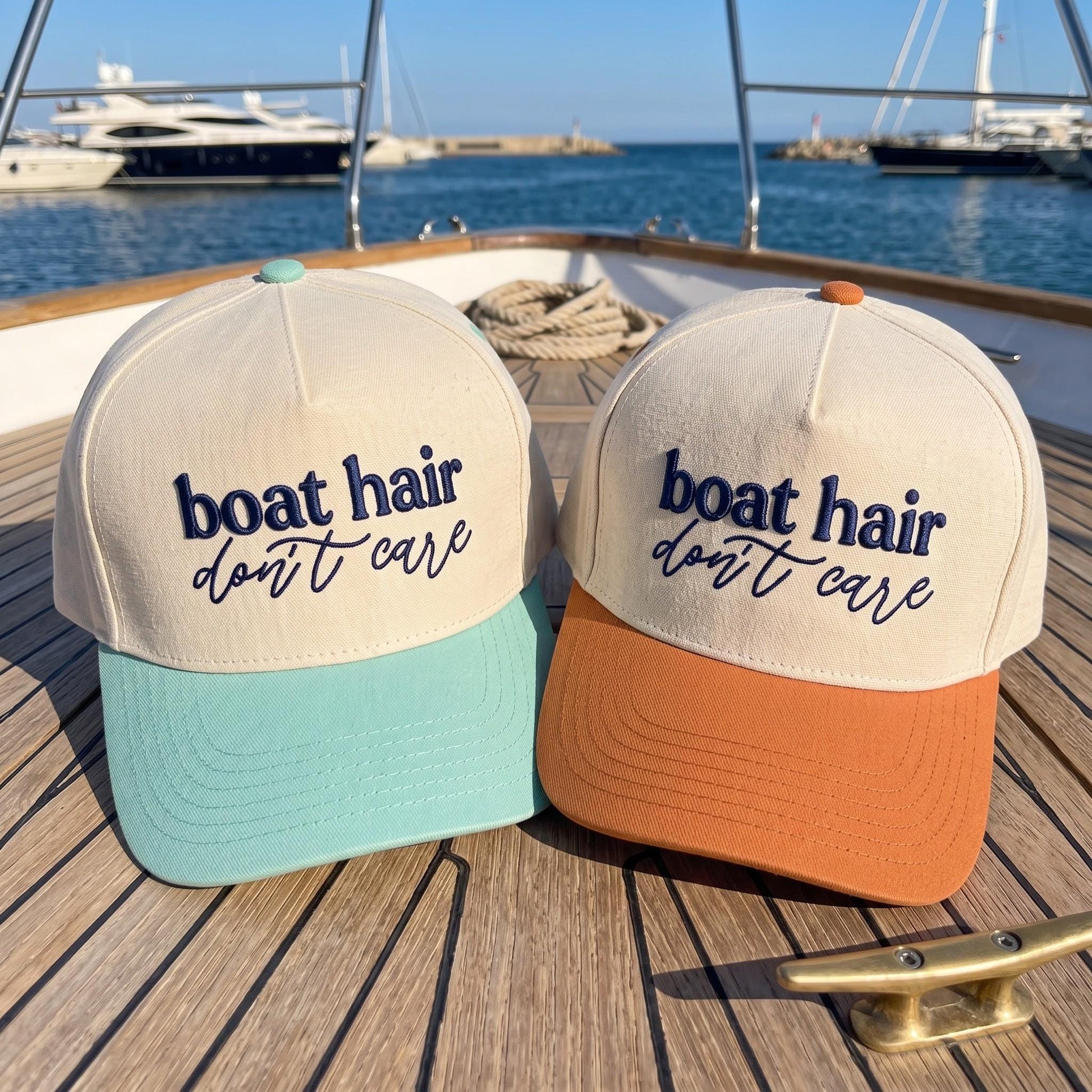 Two Boat Hair Don't Care embroidered hats with mint and orange brims on a yacht