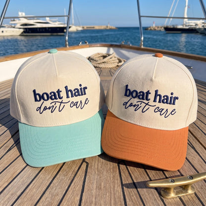 Two Boat Hair Don't Care embroidered hats with mint and orange brims on a yacht