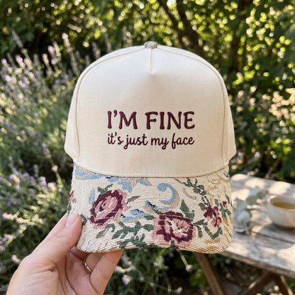 Cream embroidered hat with “I’M FINE, it’s just my face” lettering and floral brim