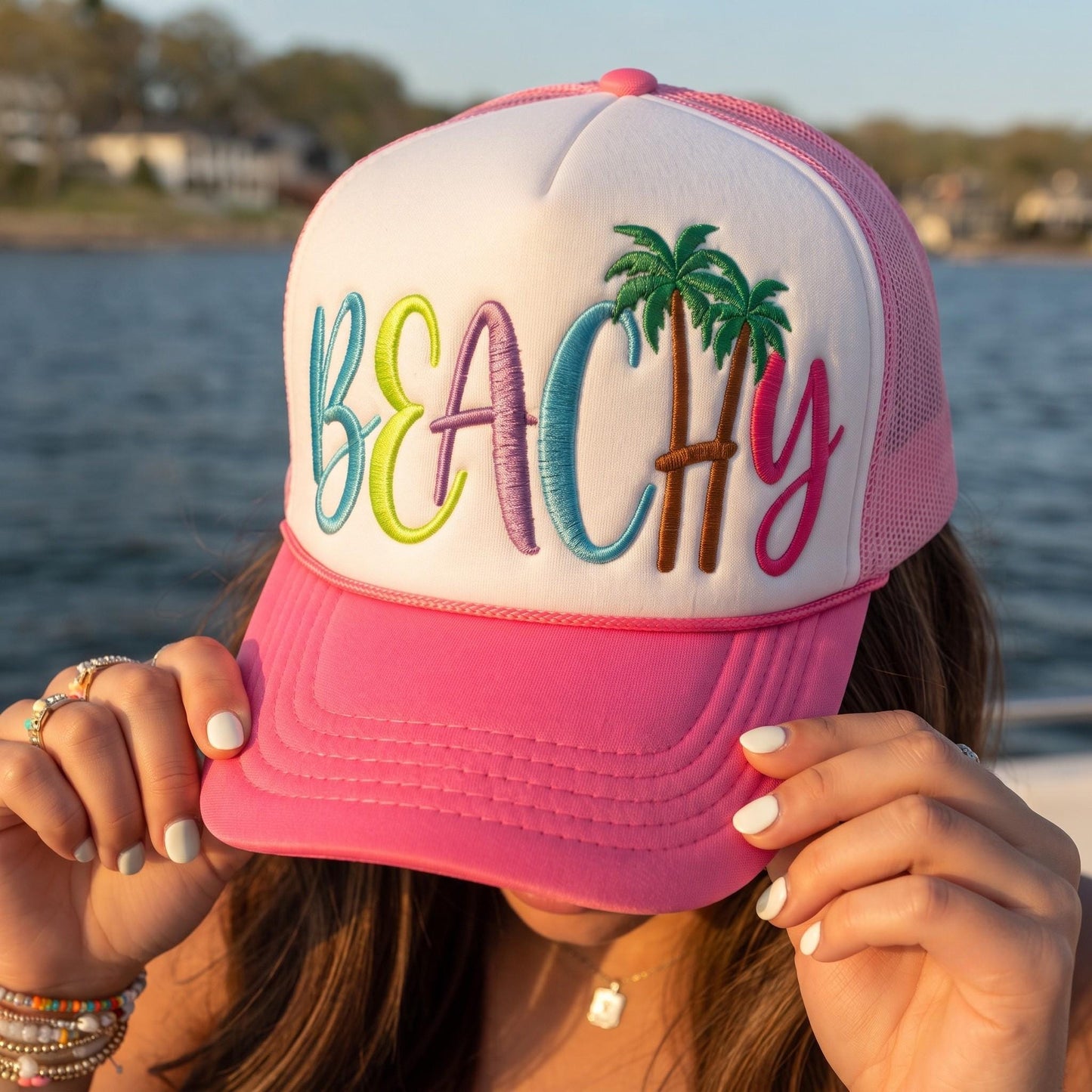 Person holding a pink beach trucker hat featuring multicolor BEACH lettering