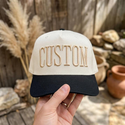 Cream and black embroidered CUSTOM hat held outdoors
