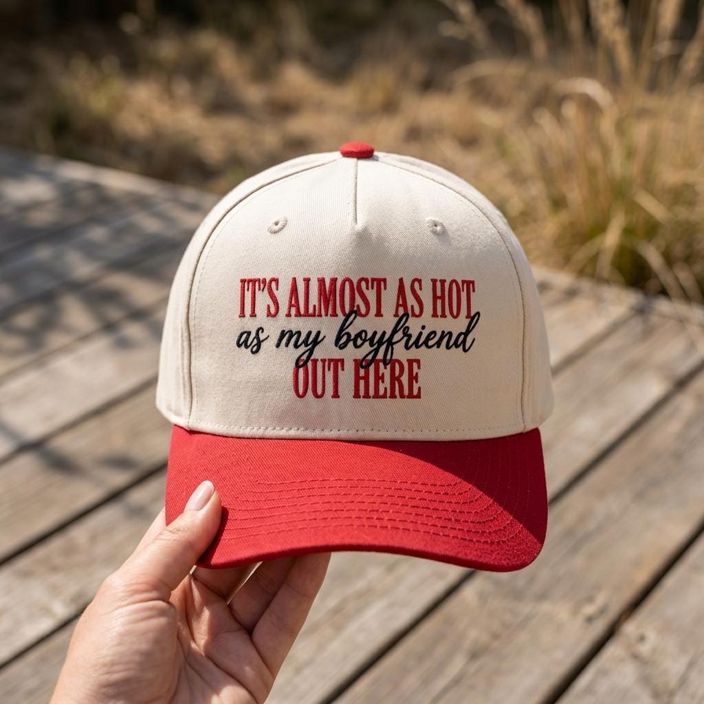 Hand holding a two-tone trucker cap with playful boyfriend quote outdoors