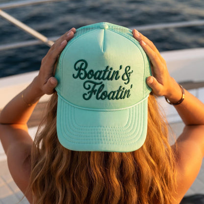 Boatin' & Floatin' aqua trucker hat shown on a boat