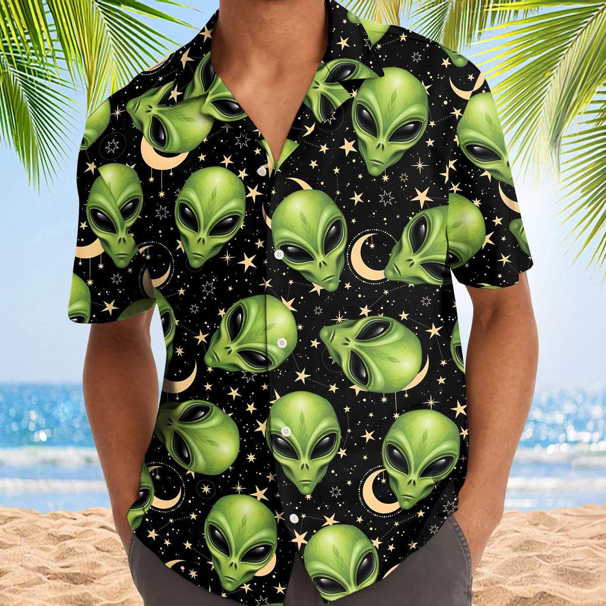 Model wearing a black alien Hawaiian shirt with green alien faces and star details at the beach