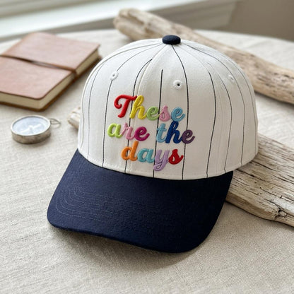 Close-up of a white pinstripe cap with multicolor embroidered lettering and navy brim
