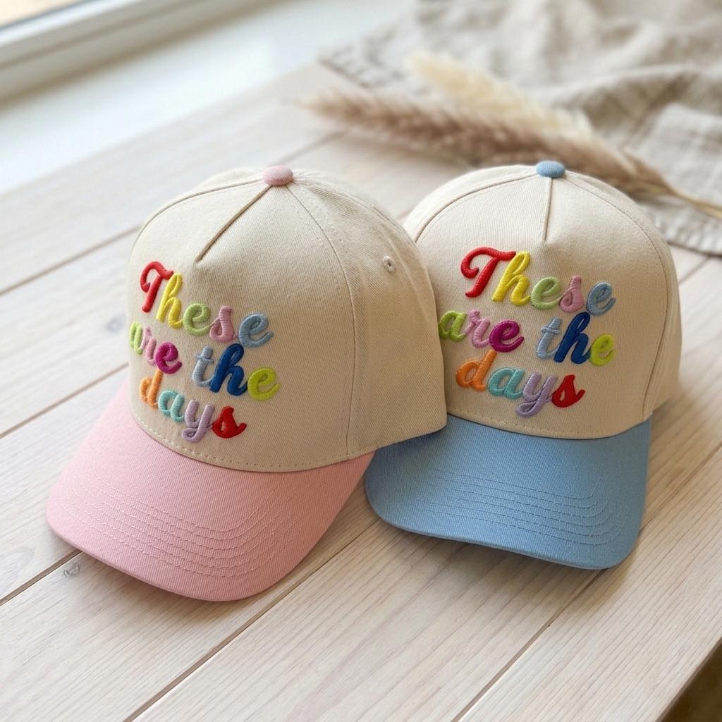 Angled view of pink and light blue brim hats with colorful embroidered lettering
