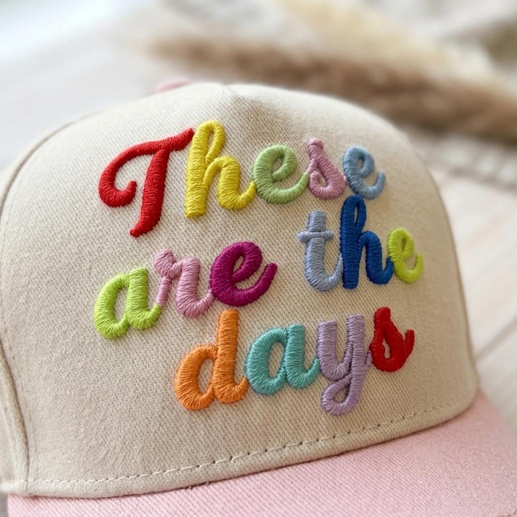 Close-up of multicolor raised embroidery reading “These are the days” on a two-tone hat