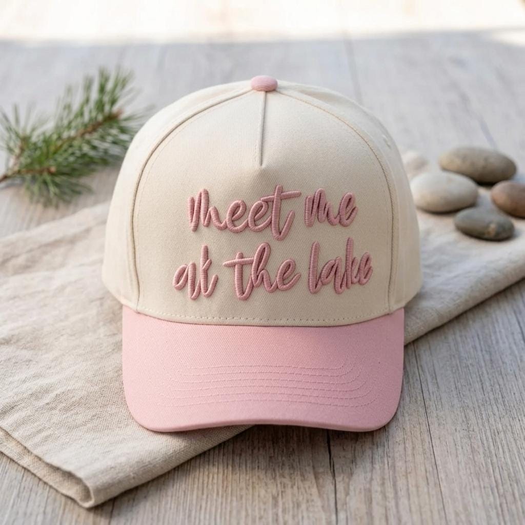 Front view of a cream and pink embroidered cap reading Meet Me at the Lake