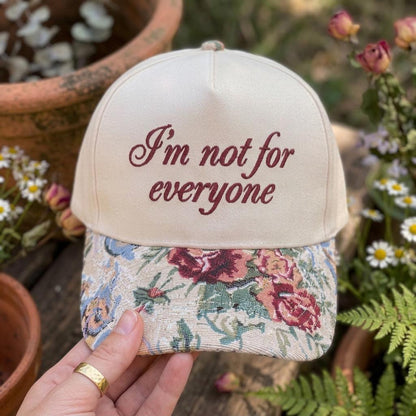 Close-up of floral brim embroidered hat held outdoors among flowers