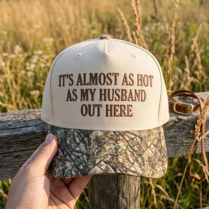 Cream hat with embroidered humorous husband saying and camouflage brim held outdoors