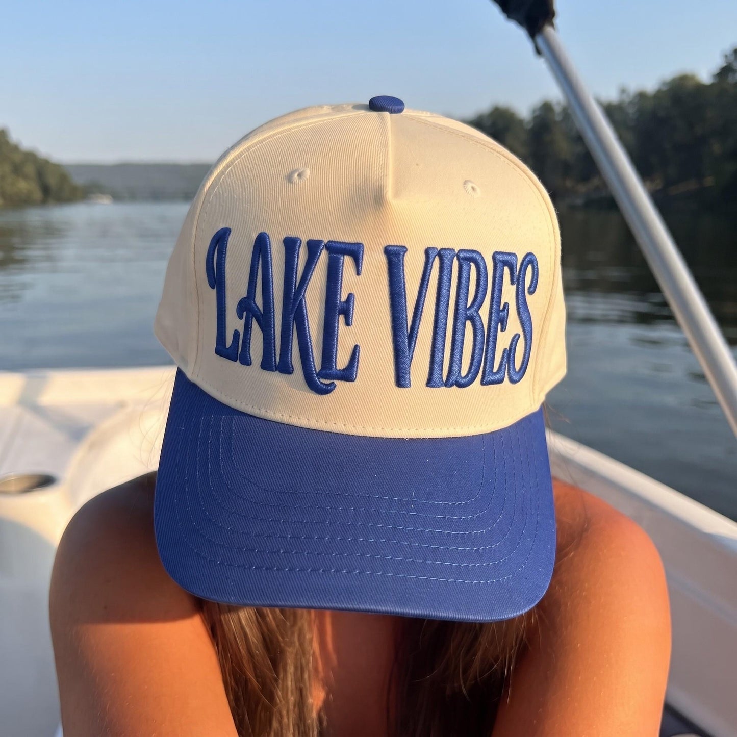 Cream and blue embroidered Lake Vibes hat photographed on a boat