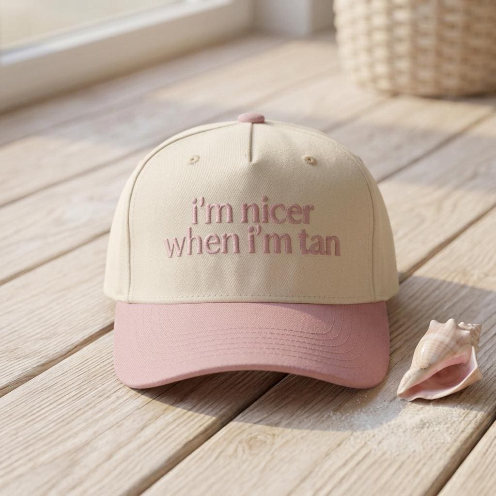 Cream and pink slogan trucker hat displayed beside seashells