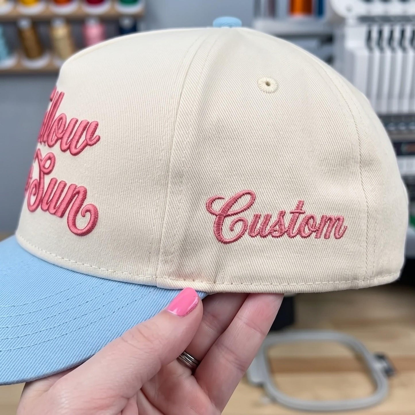 Close-up of a cream hat with pink Custom embroidery and a light blue brim
