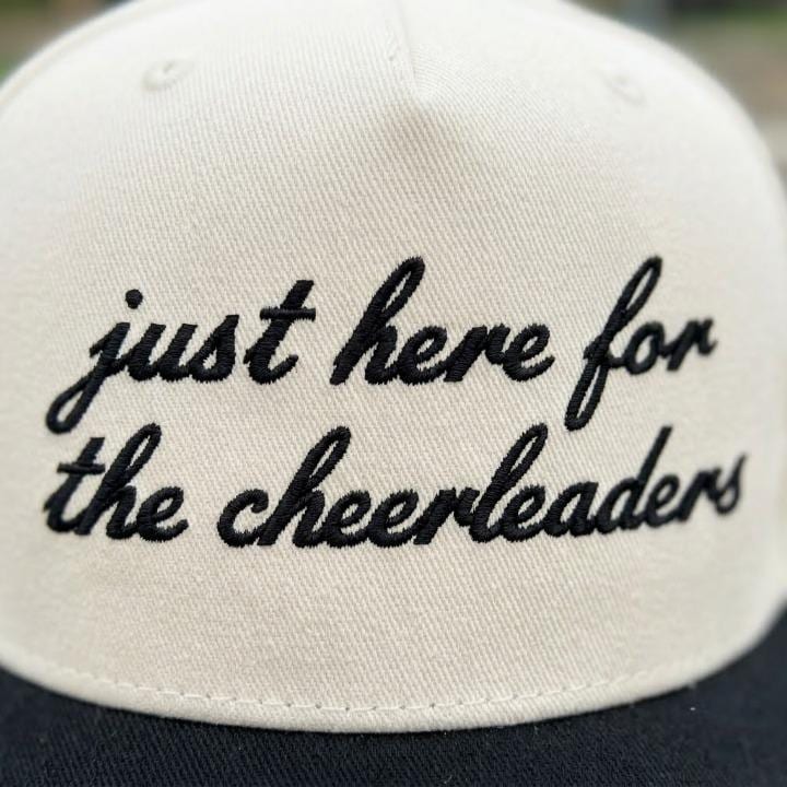 Close-up view of black script embroidery reading “just here for the cheerleaders”