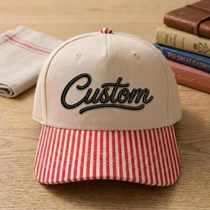 Khaki hat with black Custom script and red striped brim on a wooden table