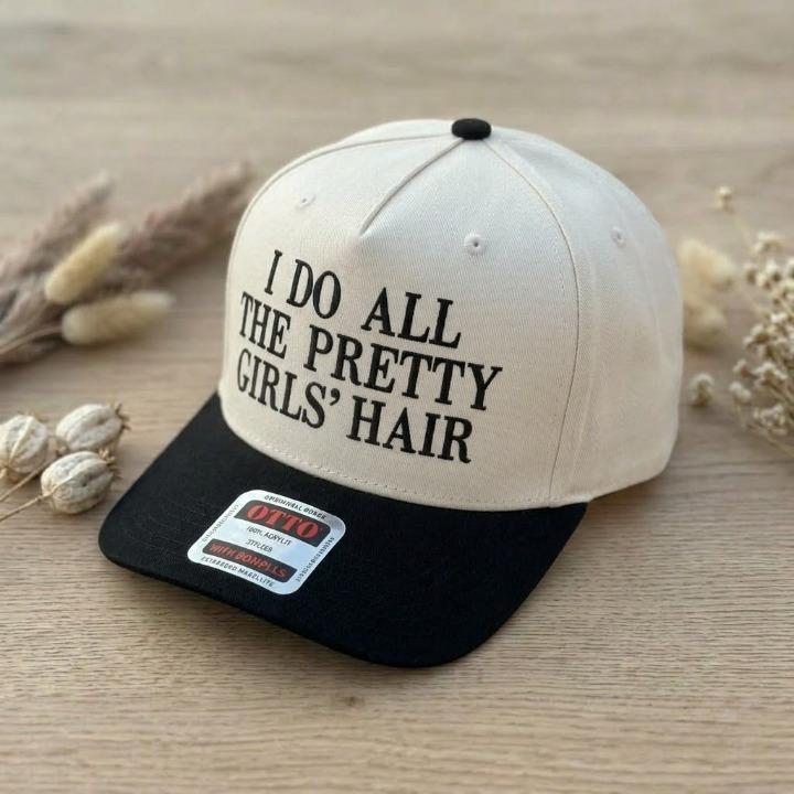 Angled view of a cream and black trucker cap with I Do All the Pretty Girls' Hair text