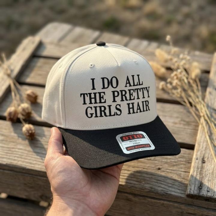 Cream and black two-tone trucker hat reading I Do All the Pretty Girls' Hair
