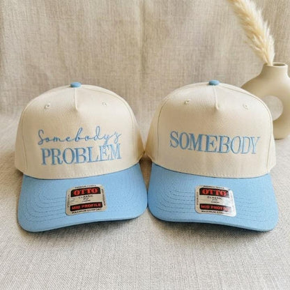 Matching cream and light blue two-tone trucker hats with Somebody’s Problem and Somebody embroidered designs
