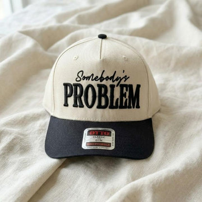 Close-up of cream and black Somebody’s Problem embroidered trucker hat