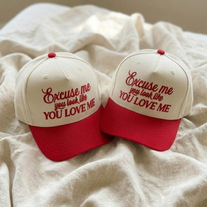 Two cream and red embroidered trucker caps displaying the phrase Excuse me, you look like you love me