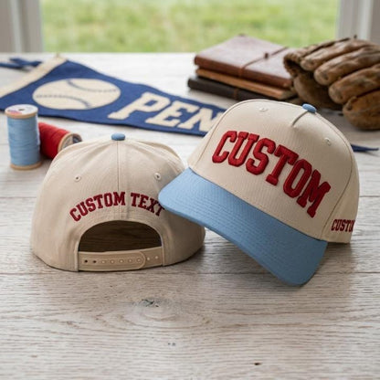 Front and back views of a cream custom baseball cap with blue brim and bold red lettering