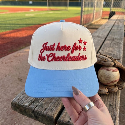 Embroidered cheerleader hat with red script lettering, star accents, and a light blue brim at a baseball field