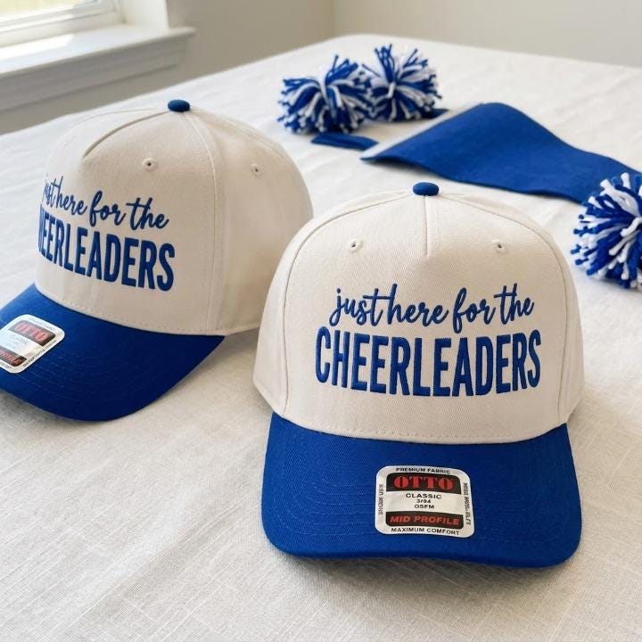 Cream and blue cheer hat displayed with blue and white pom poms