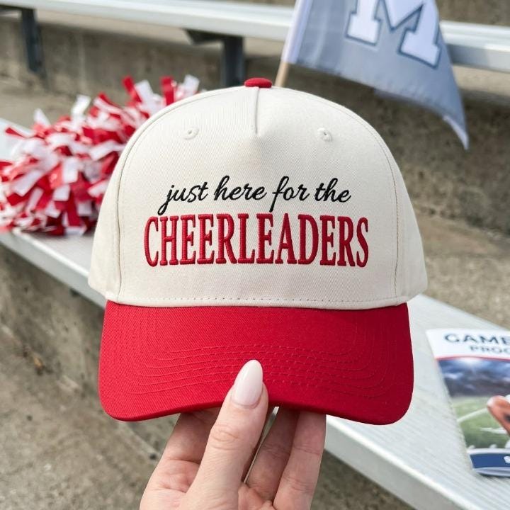Cream and red two-tone trucker cap embroidered with “just here for the CHEERLEADERS”