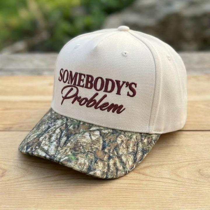 Angled view of Somebody’s Problem hat showing the cream crown and camo bill