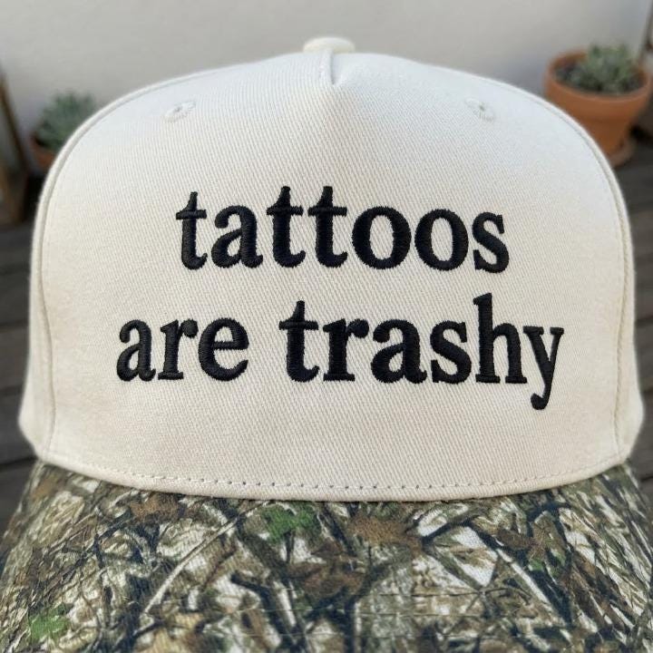 Close-up of black “tattoos are trashy” embroidery on cream hat front
