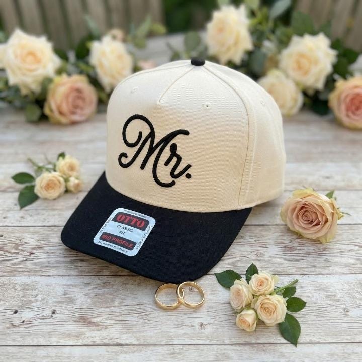 Cream and black Mr. embroidered hat shown with wedding flowers