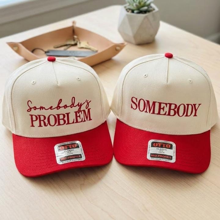 Matching cream and red two-tone trucker hats with Somebody’s Problem and Somebody front lettering