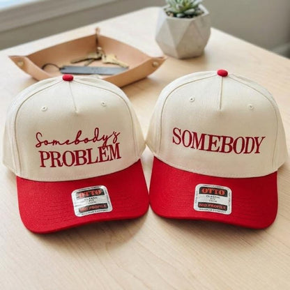Matching cream and red two-tone trucker hats with Somebody’s Problem and Somebody front lettering