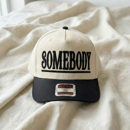 Close-up of cream and black Somebody embroidered trucker hat