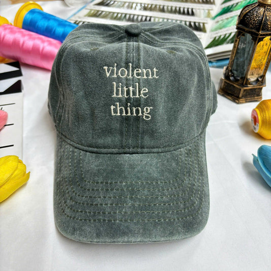 Washed dark green dad hat with embroidered quote “violent little thing” in off-white thread – minimalist and edgy fashion piece